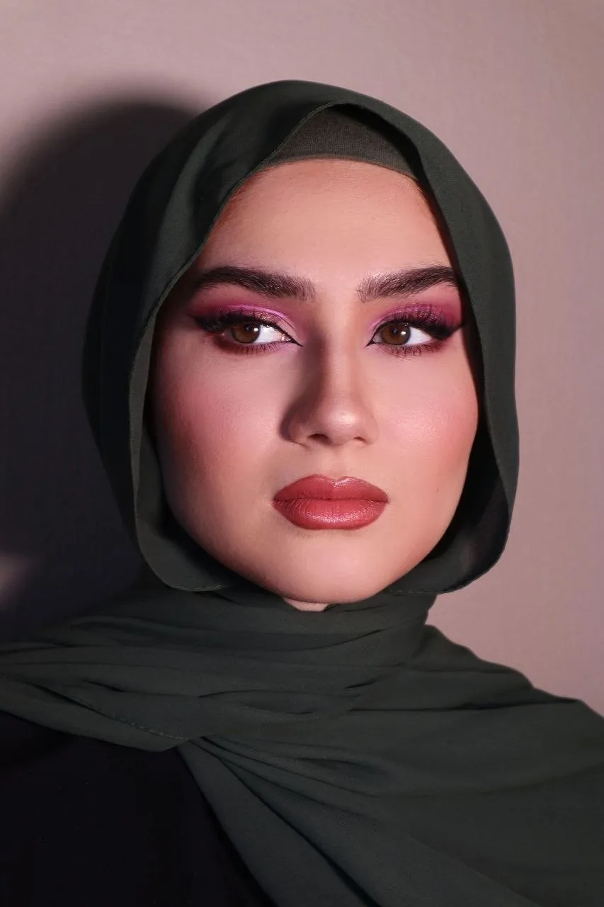 Portrait in an olive hijab with a bright fuchsia halo eye, matching blush and a glossy terracotta lip.