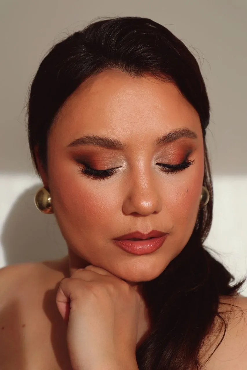 Close-up of a warm terracotta smoky eye with a sharp wing, on glowing skin, with gold earrings.