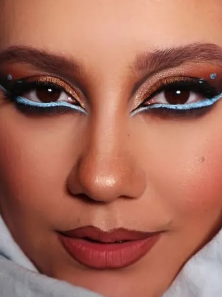 Close-up of a copper glitter eye with pale blue graphic liner above and below, and small crystals at the corners.